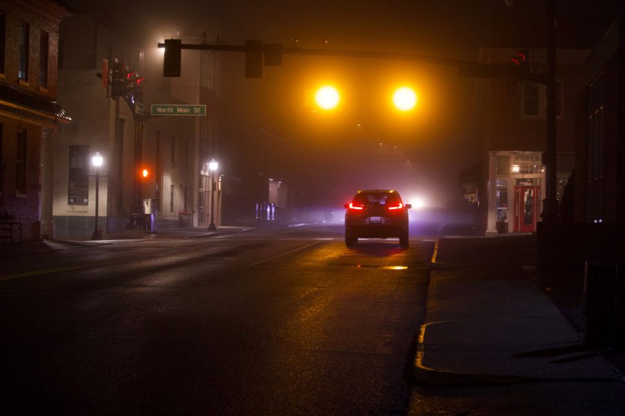 A small town Main St. traffic light intersection at night with a dark car stopped