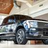 A black 2022 Ford F-150 Lightning Lariat parked inside a dealer showroom in low right front angle view