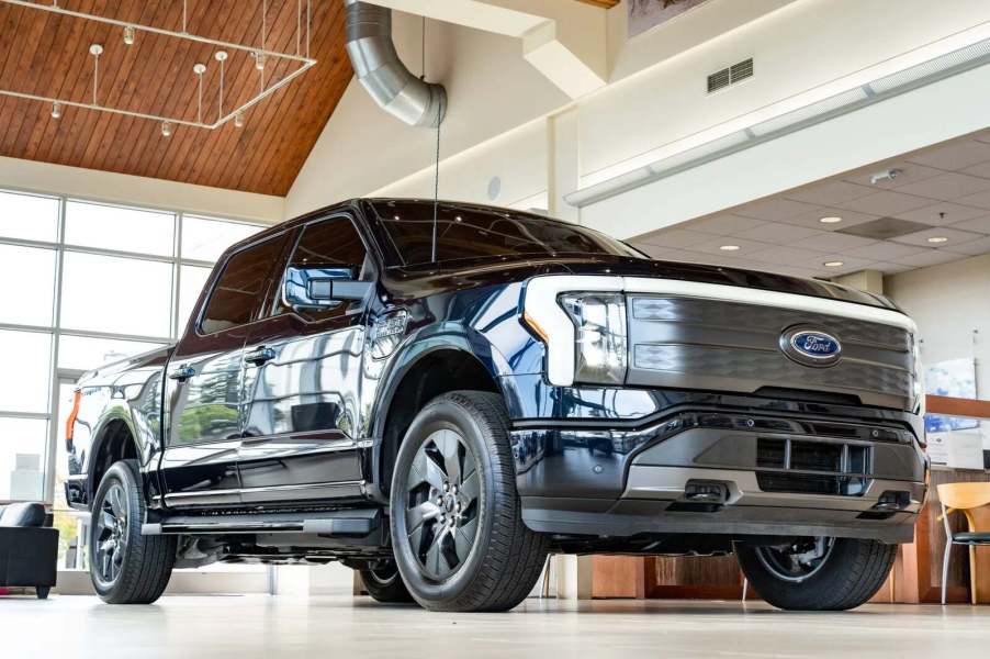 A black 2022 Ford F-150 Lightning Lariat parked inside a dealer showroom in low right front angle view