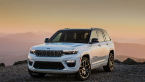 A white 2024 Jeep Grand Cherokee 4xe parked in left front angle view at dusk