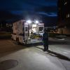 Man stands behind an open, empty ambulance in a parking lot at night.