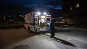 Man stands behind an open, empty ambulance in a parking lot at night.