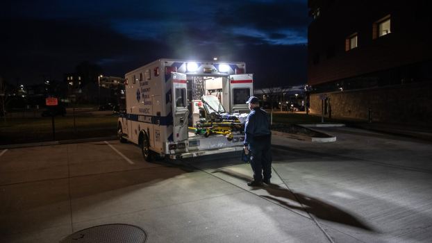 Man stands behind an open, empty ambulance in a parking lot at night.