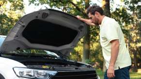 Man looks under hood, at engine of car.