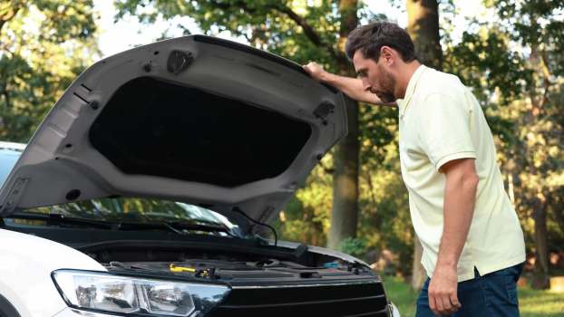 Man looks under hood, at engine of car.