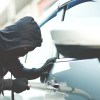 Thief in a hood and mask uses a screwdriver to get into a silver sedan