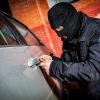 Thief in mask breaks into a silver car, a brick wall visible in the background.