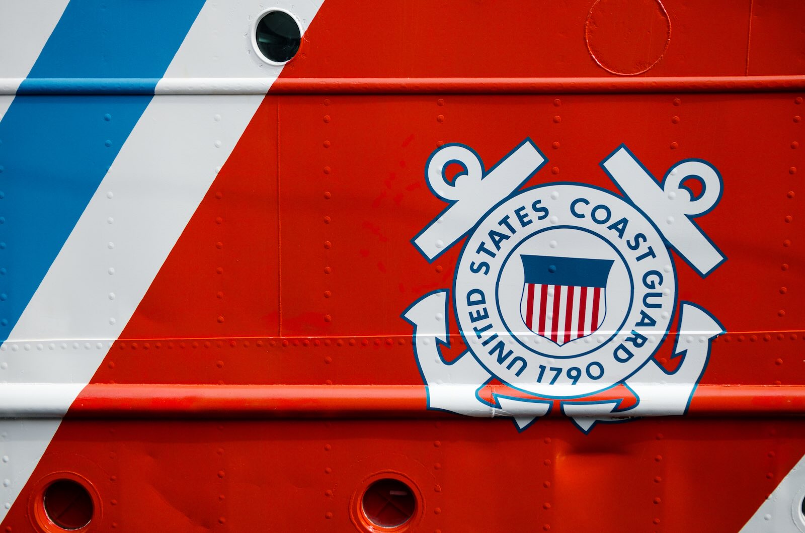 The United States Coast Guard seal on the orange and blue hull of a ship.