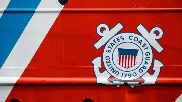 The United States Coast Guard seal on the orange and blue hull of a ship.