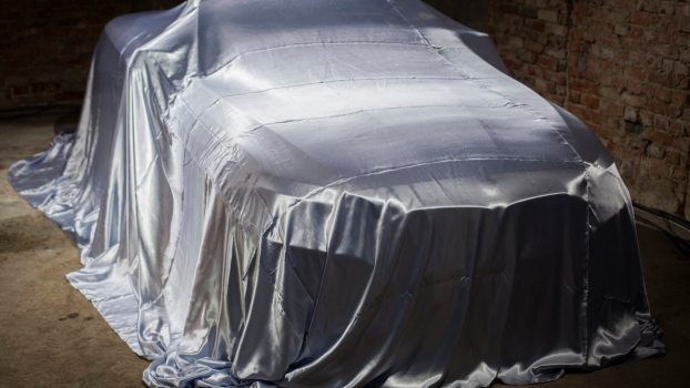 Collector car under cover in front of a brick wall.