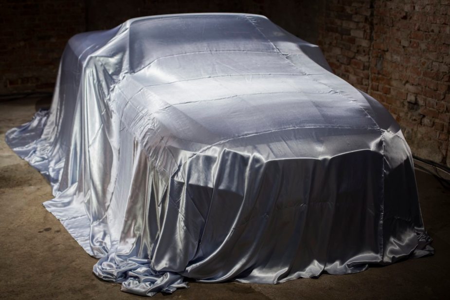 Collector car under cover in front of a brick wall.