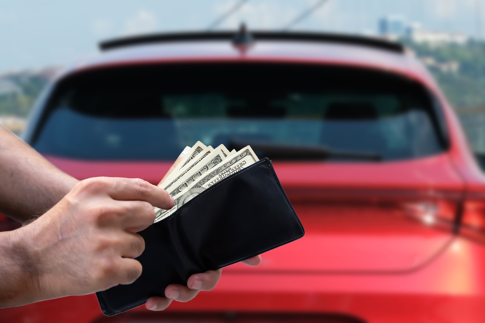 Car buyer pulls out cash, a red crossover SUV in the background.