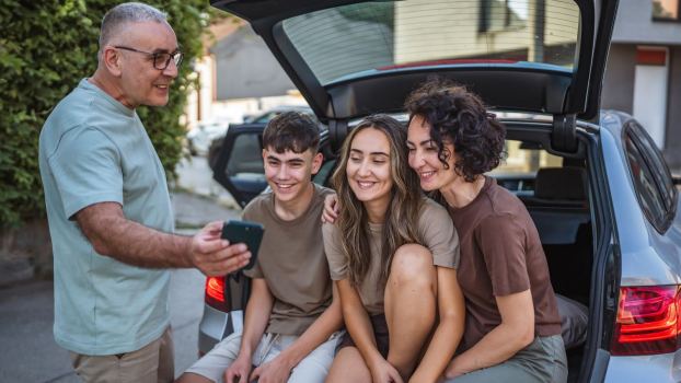 Family poses for a selfie on the tailgate of their SUV.