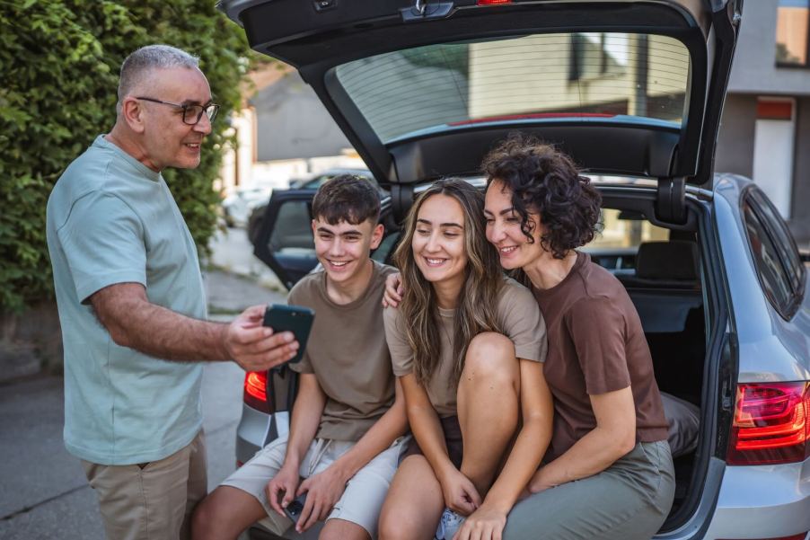 Family poses for a selfie on the tailgate of their SUV.