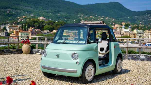 Green Fiat Topolino quadricycle car parked in front of a harbor in Italy.