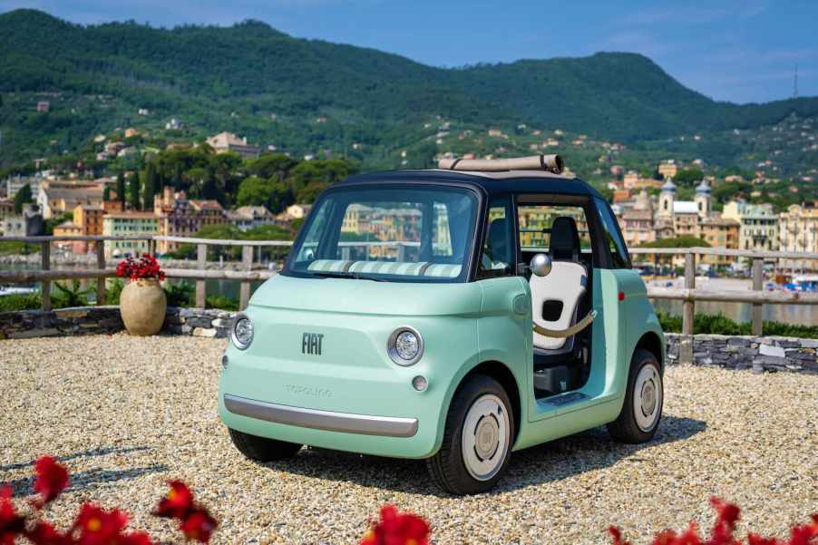 Green Fiat Topolino quadricycle car parked in front of a harbor in Italy.