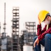 Factory worker in a yellow hard hat sits in front of a plant