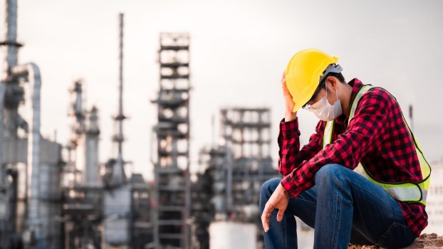 Factory worker in a yellow hard hat sits in front of a plant