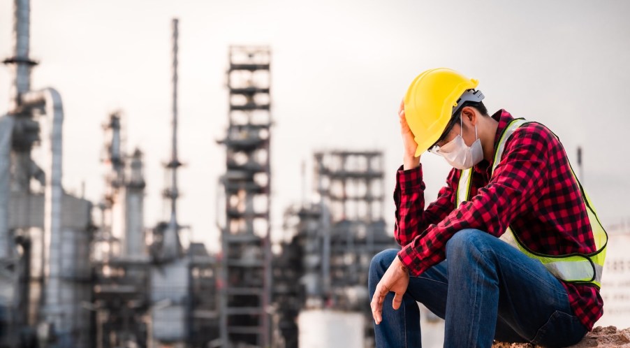 Factory worker in a yellow hard hat sits in front of a plant