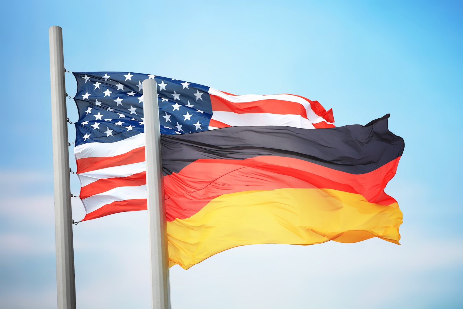 German flag against a blue sky, U.S. national flag in the background.