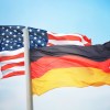 German flag against a blue sky, U.S. national flag in the background.