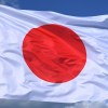 White Japanese flag with a bright red dot, in front of a blue sky.