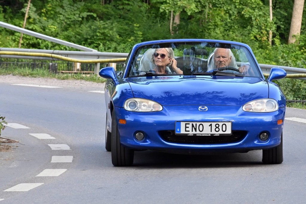 Couple drives a blue Mazda Miata convertible sports car on a winding road