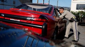 California Highway Patrol officer leans into the window of a red sport car during a traffic stop.