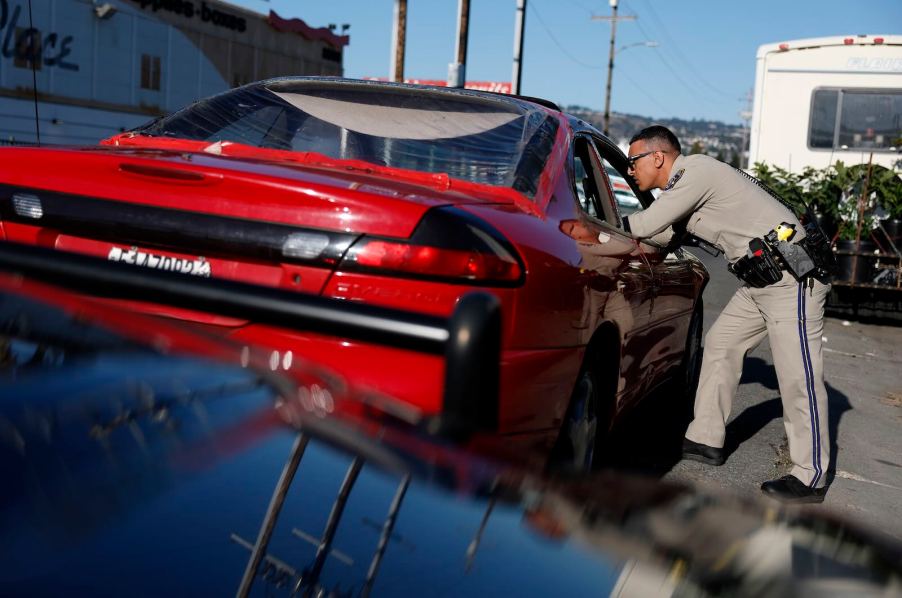 California Highway Patrol officer leans into the window of a red sport car during a traffic stop.