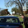 Police officer leans over to speak with a passenger in a blue Honda Civic during a traffic stop, trees visible in the background.
