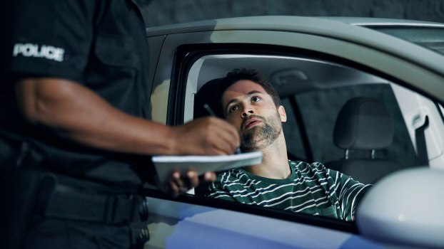Driver looks up at a police officer who's standing by his car and writing a speeding ticket