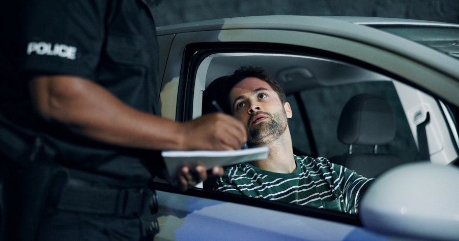 Driver looks up at a police officer who's standing by his car and writing a speeding ticket