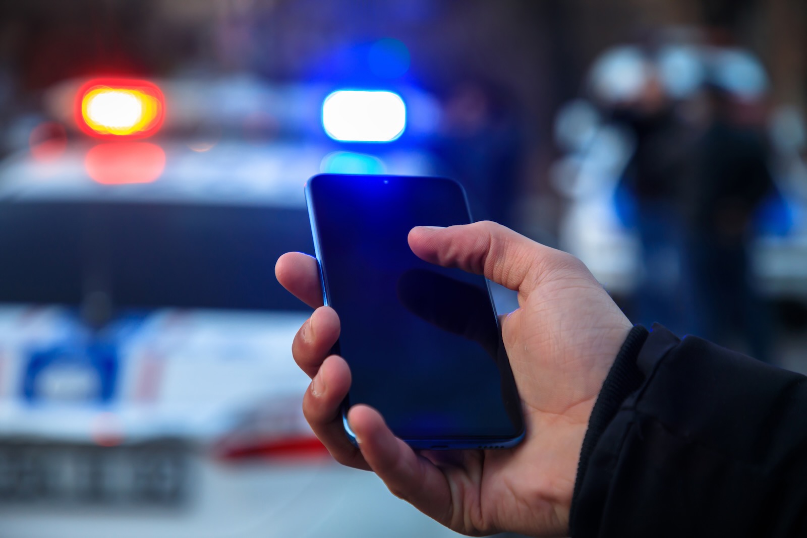 Police officer stands in front of a cruiser while searching a suspect's iPhone