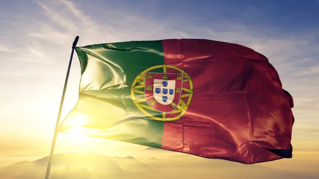 the Portuguese national flag waving in front of a sunset