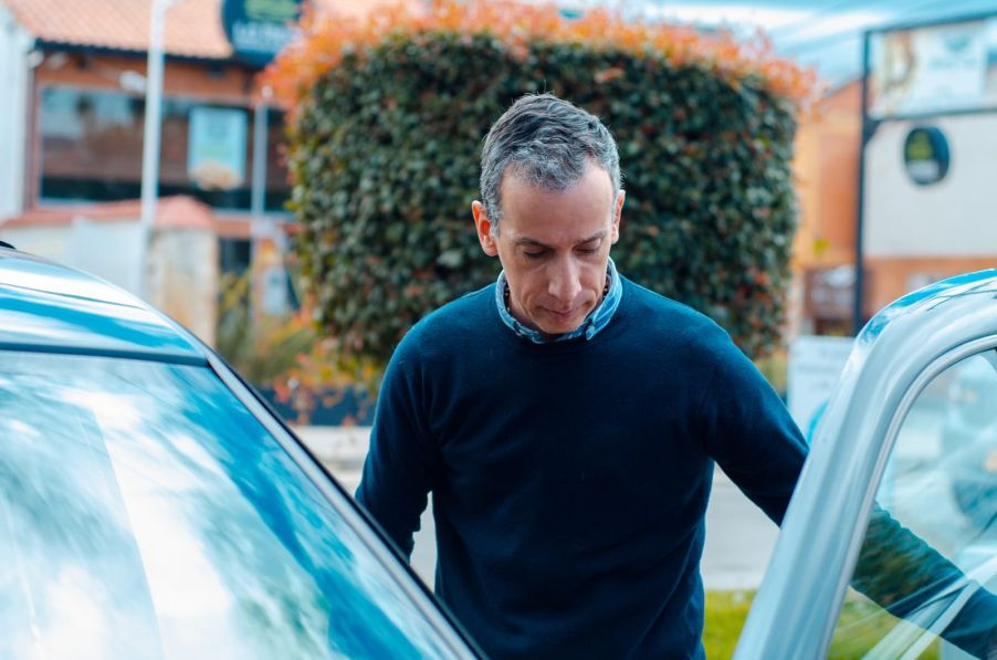 Man studies the inside of his car door, with the door open.
