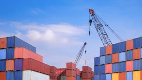 Tall st asks of shipping containers with cranes visible in the background.