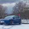 Blue Tesla Model 3 charging during the winter, snow visible in the foreground.
