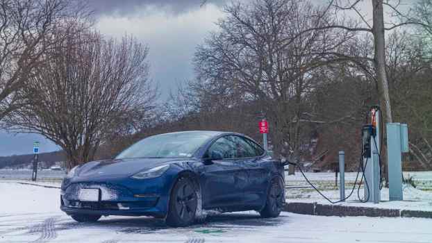 Blue Tesla Model 3 charging during the winter, snow visible in the foreground.
