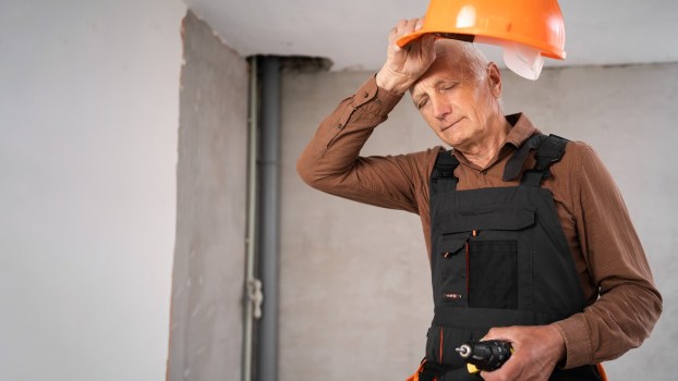 Tired construction worker takes off his helmet to wipe his forehead.