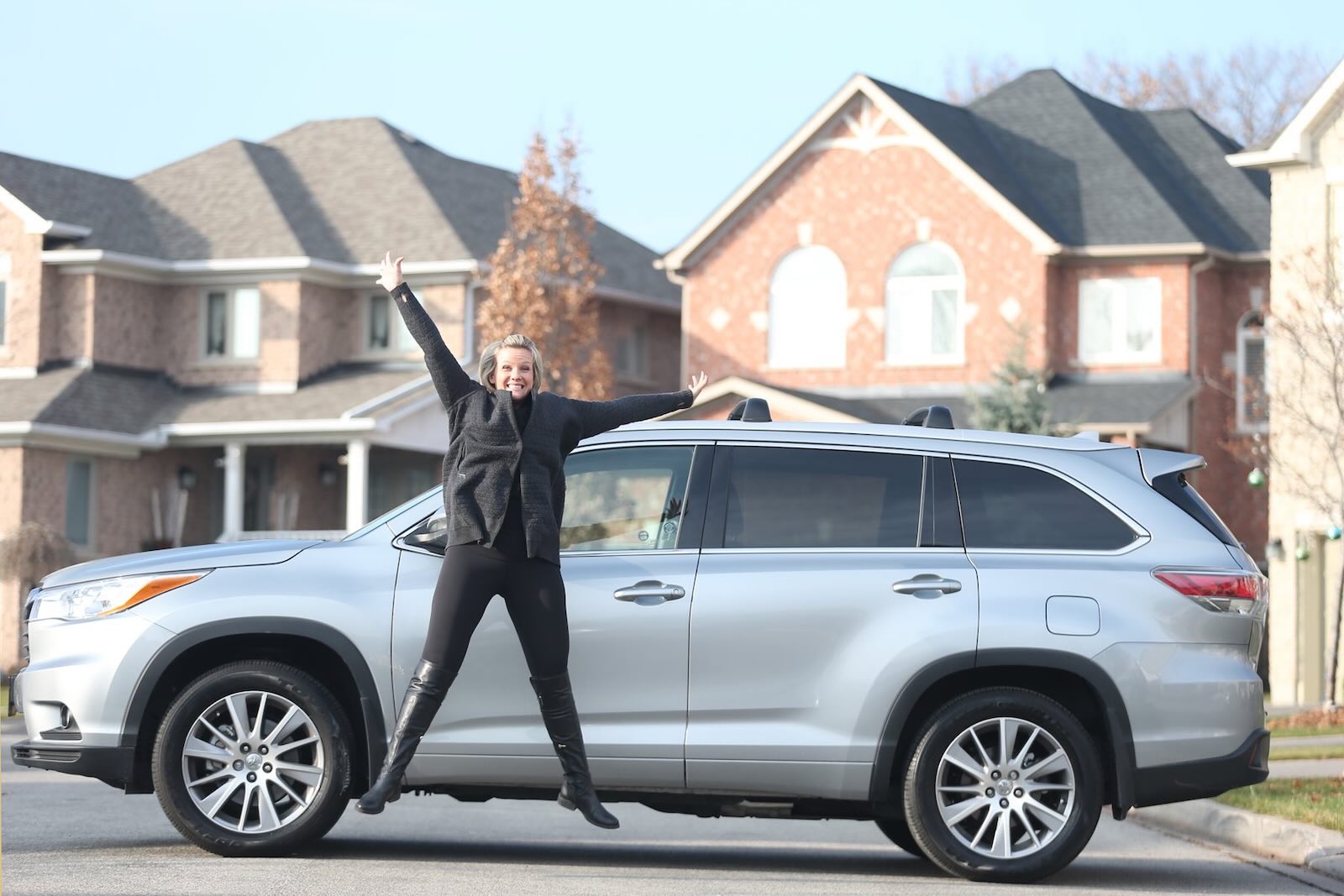 Woman jumps in the air in front of her silver Toyota Highlander SUV