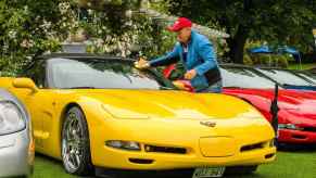 Yellow Chevy Corvette parked at a car show, its owner cleaning off the windshield with a rag.