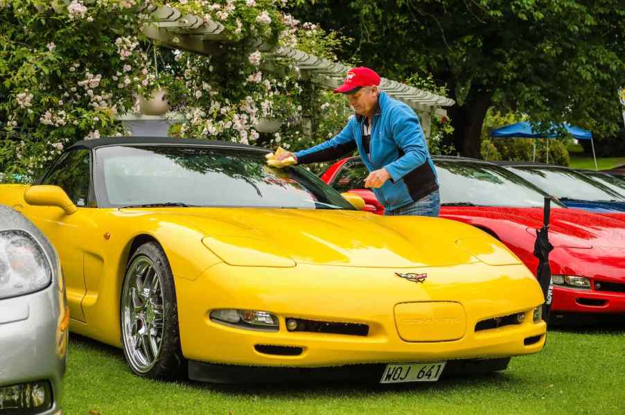 Yellow Chevy Corvette parked at a car show, its owner cleaning off the windshield with a rag.