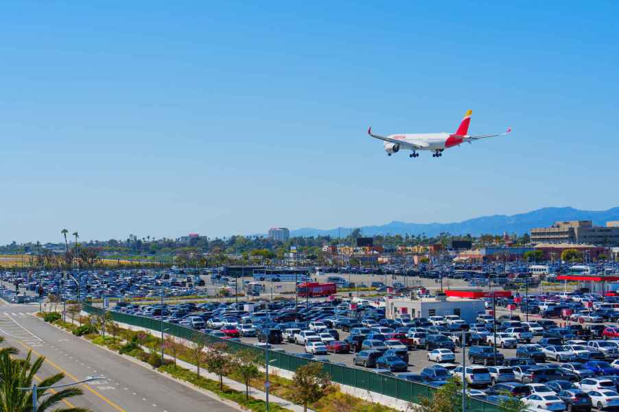 An airport parking lot with commercial jet flying over