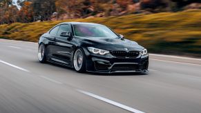 A black BMW M4 driving fast on a highway in right front angle view
