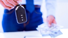 A car salesman holds a ley fob in one hand and cash in another view of waist