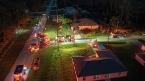 Emergency vehicles with lights on parked in front of a home from aerial view