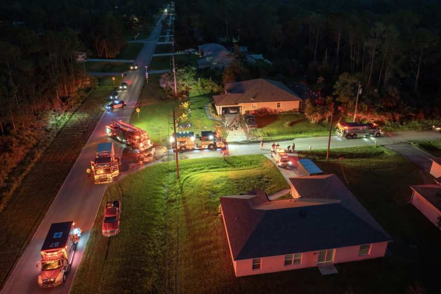 Emergency vehicles with lights on parked in front of a home from aerial view