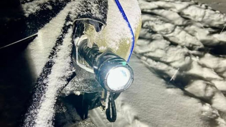 A snow-covered car in Wisconsin with the left headlamp broken and a flashlight strapped in to replace it, shown in very close view