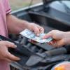 Handing a mechanic cash with car behind in close view of their hands