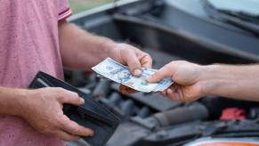 Handing a mechanic cash with car behind in close view of their hands
